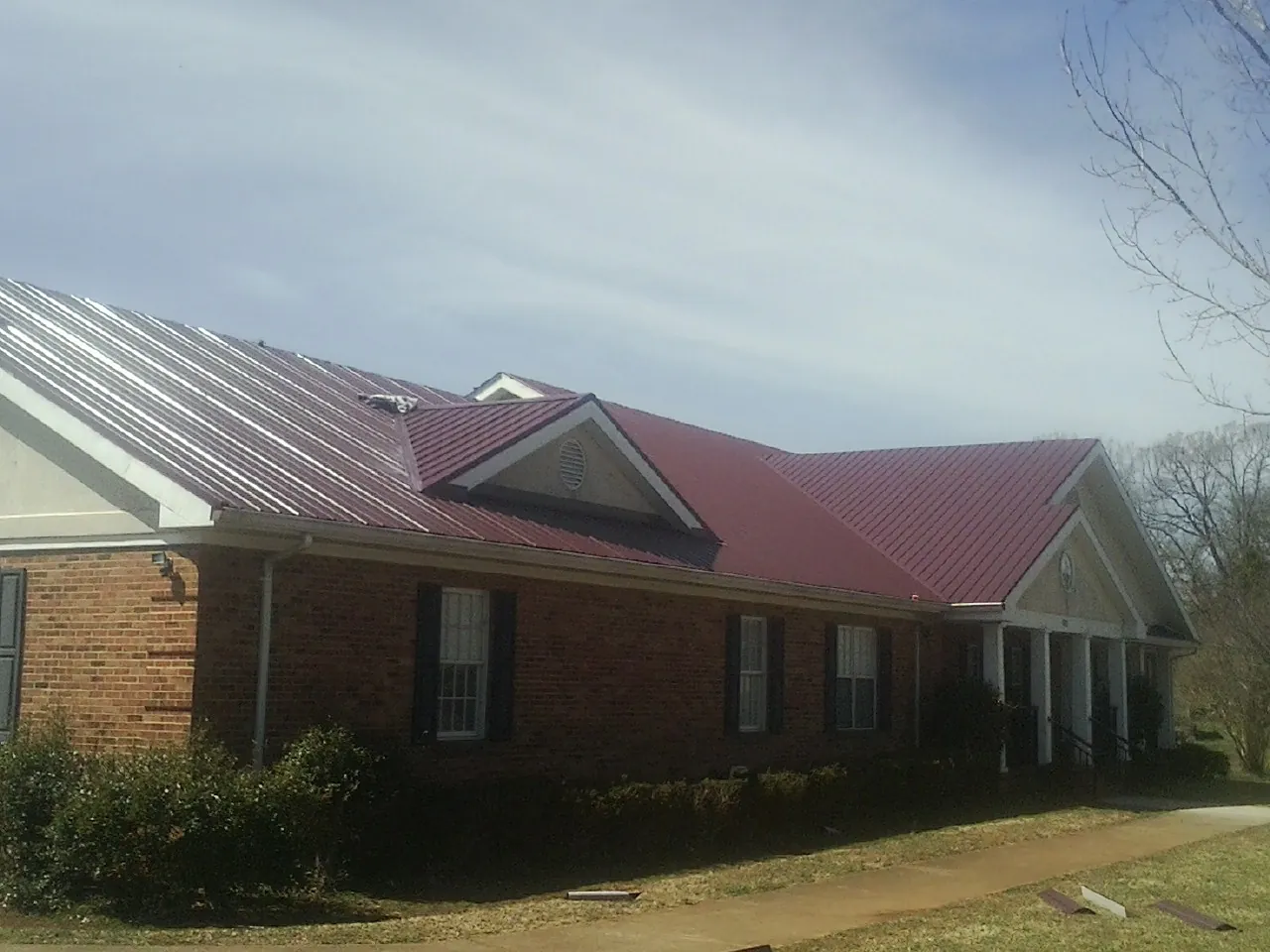 Red metal roof with gabled entries on a long brick building, from a Hail Damage Roof Repair job in Searcy