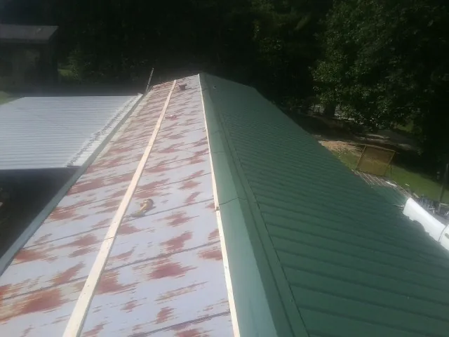 Old rusted panels beside newly installed green metal roofing — Wind Damage Roof Repair by Roofing Brothers in Searcy