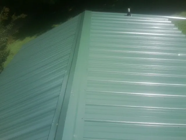 New green metal panels meeting at the ridge of a roof — Flat Roof Repair work by our crew in Searcy