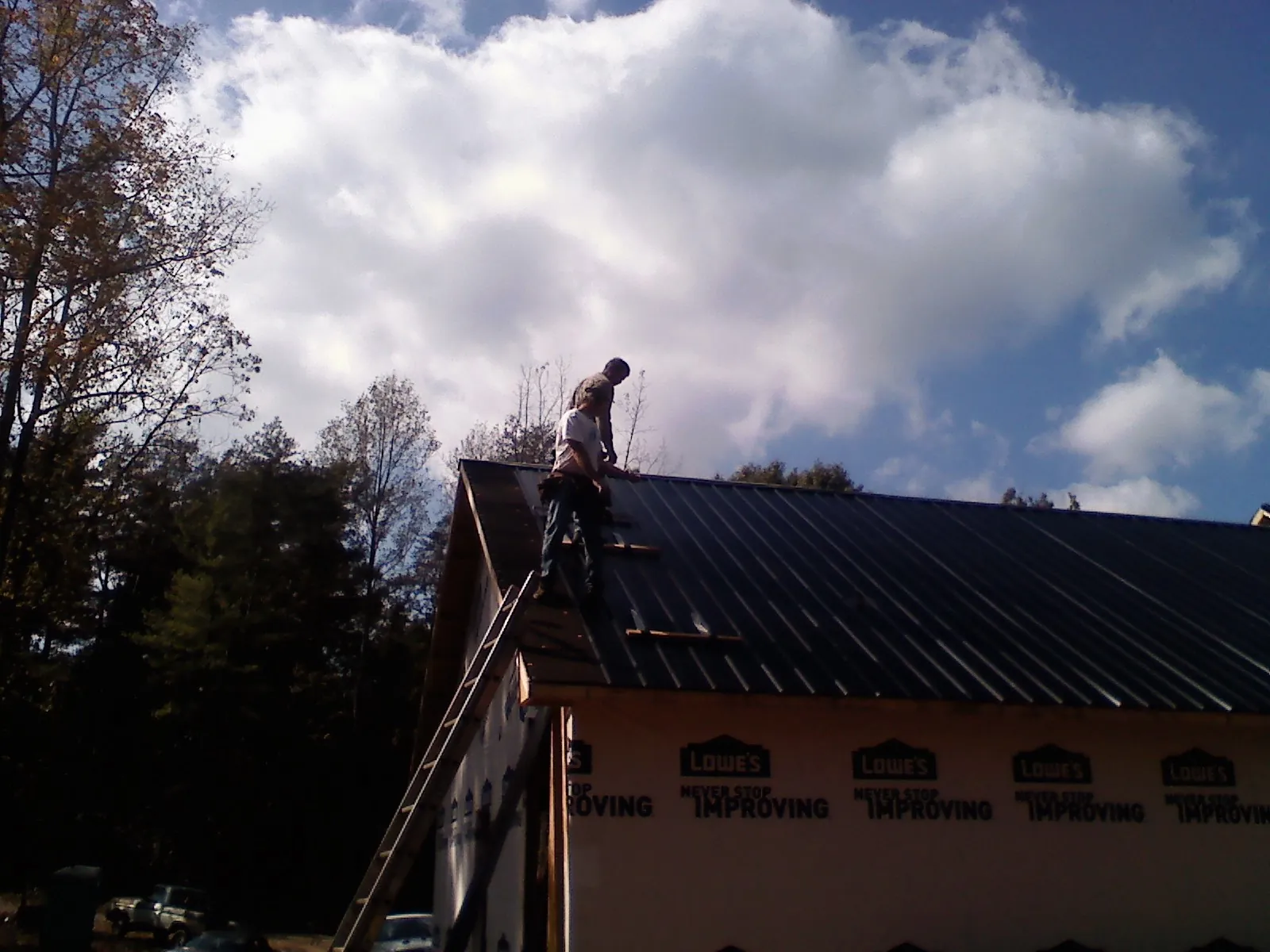Roofer fastening dark metal panels high against a cloudy sky, from a Roof Inspection job in Searcy