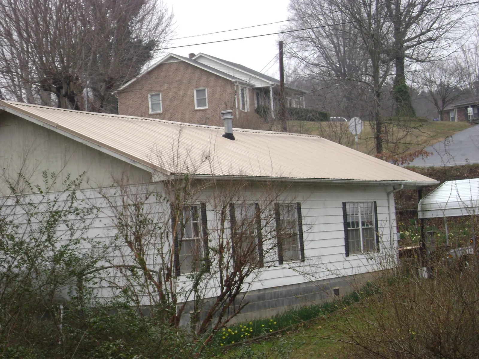 Tan metal roof on a white sided house set into a hillside — Commercial Roofing by Roofing Brothers in Searcy
